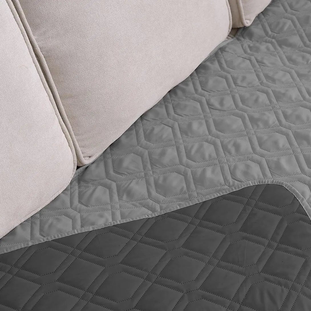 Quilted Sofa Protector in Mist — reversible quilted cover draped over a sofa seat, showing the light and dark sides